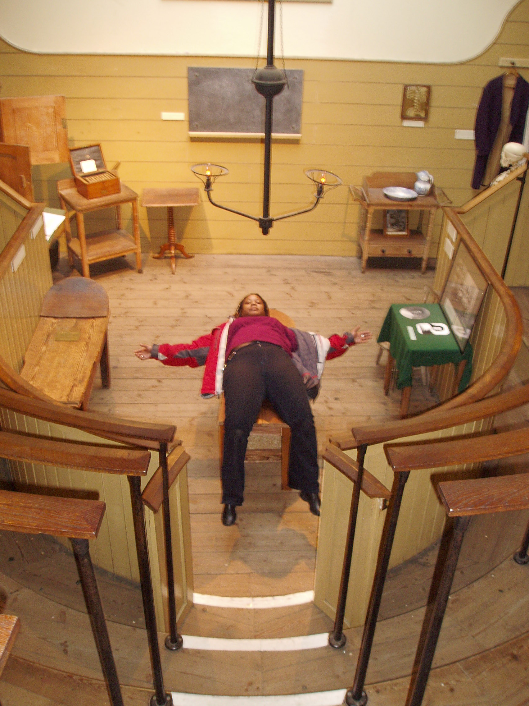 the women's operating room in London, UK, with Anita lying on the operating table in the middle, her head raised, looking at the camera. Her arms are spread out into a cross-shape. Around her, the theatre curves up, the benches where medical students would have sat to stare at the procedures.